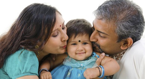 Mother and father each side of a baby each kissing the cheek of the baby